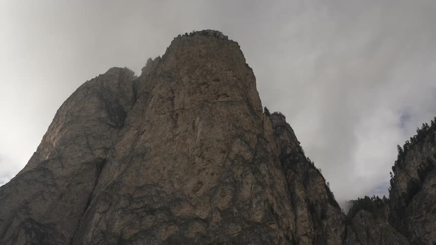 A dramatic time-lapse of swirling fog and clouds moving over a towering rocky mountain peak