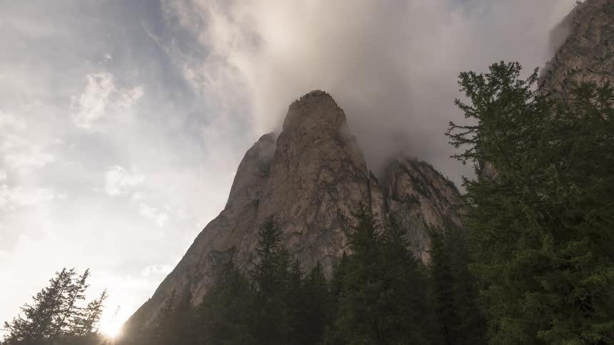 A dramatic timelapse captures clouds swirling around a rugged mountain peak as the sun rises