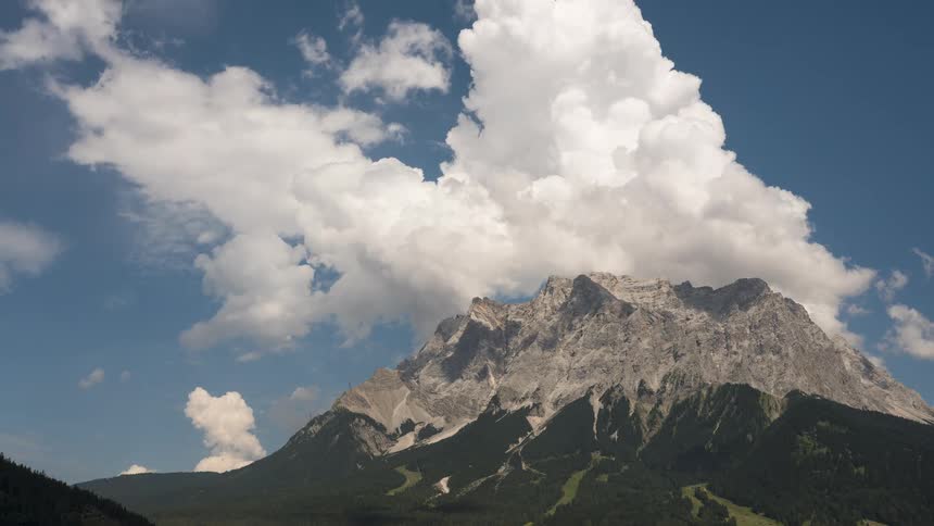 A time-lapse of fluffy white clouds drifting slowly over a majestic, rugged mountain peak against a bright blue sky