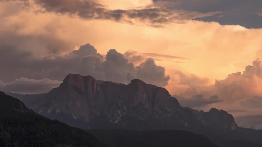 Stunning sunset timelapse shows billowing clouds changing from golden to pink over the silhouette of a mountain range