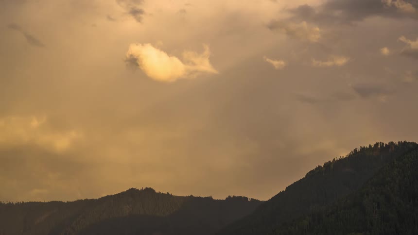 A beautiful rainbow arcs over a mountain ridge and disappears as the golden sky fills with dramatic clouds