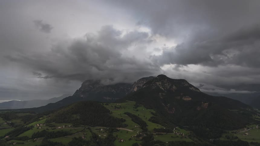 A dramatic time-lapse of a powerful thunderstorm with lightning flashing in dark clouds rolling over a mountain range and valley