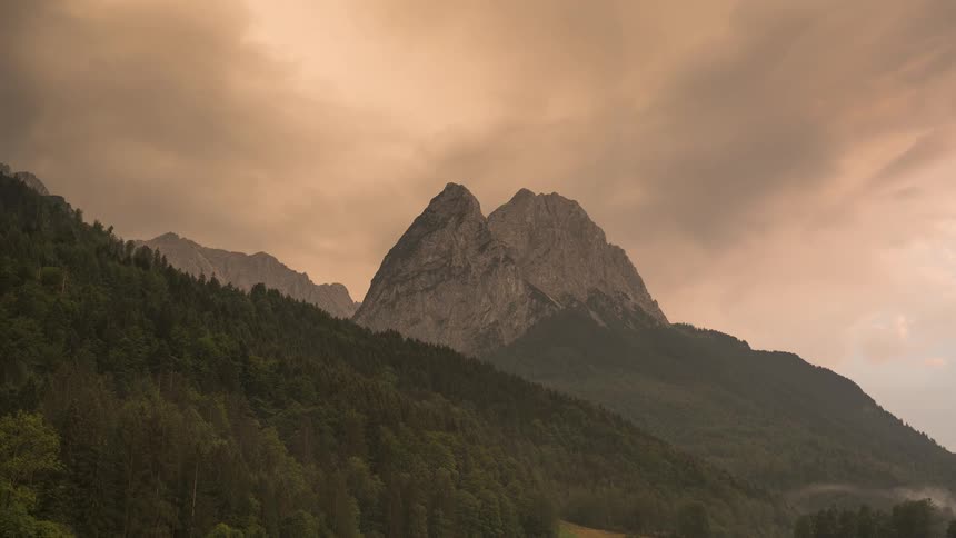A stunning timelapse of fog and clouds swirling around forested mountain peaks during a dramatic sunset