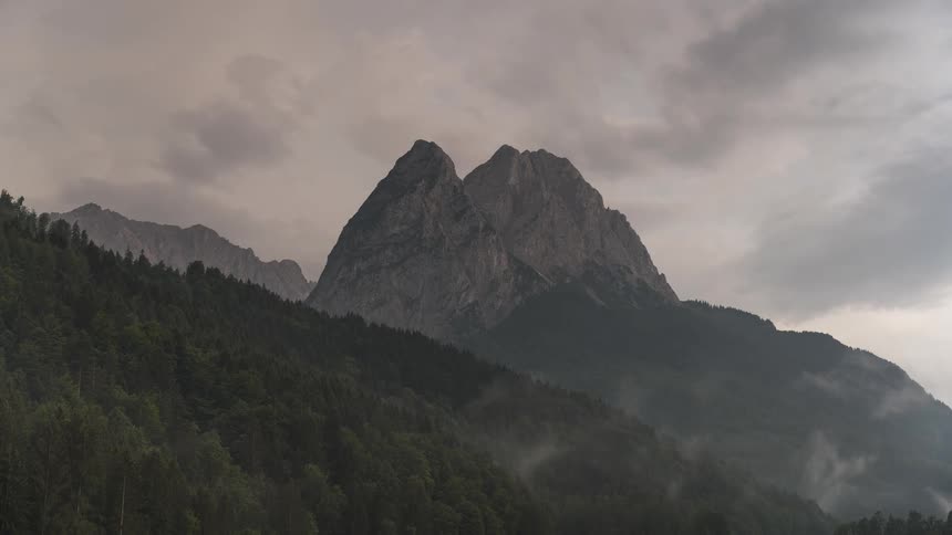 A dramatic timelapse of moody fog and clouds rolling over a forested twinpeaked mountain range