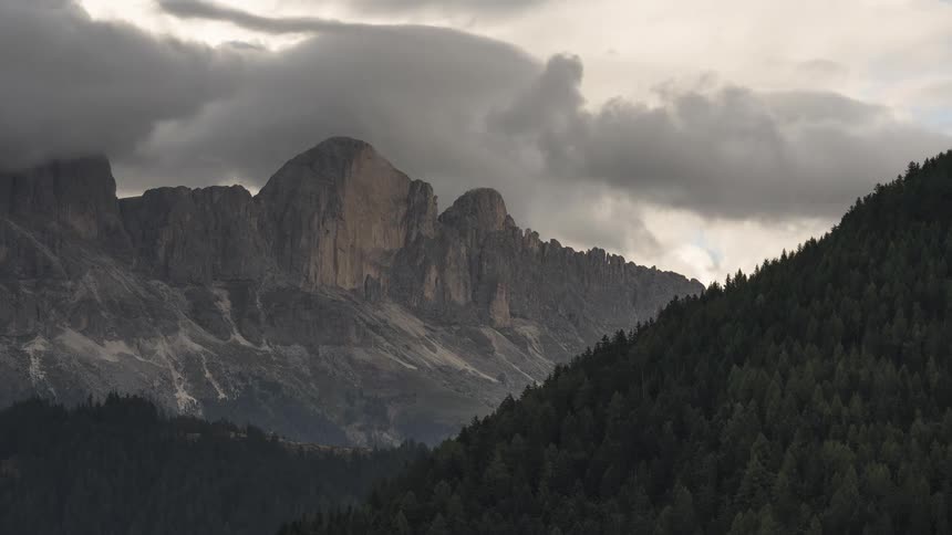 Dramatic dark clouds drift over a rugged mountain range and a vast evergreen forest