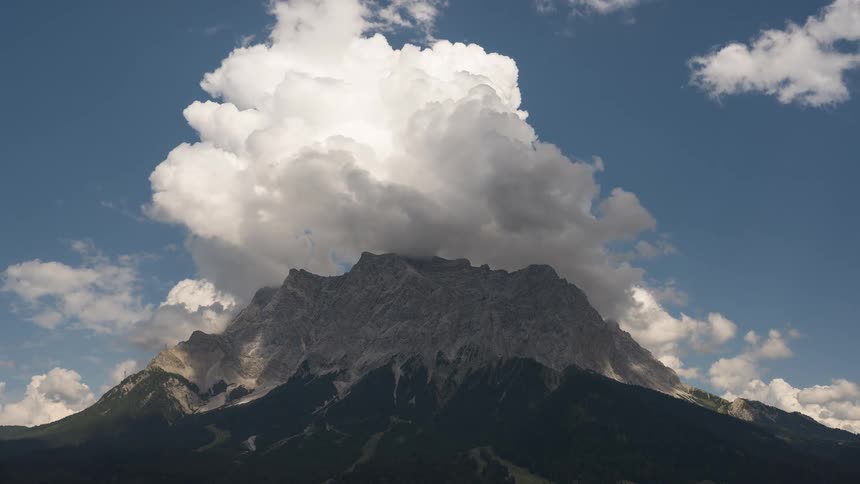 A dramatic timelapse captures billowing white clouds forming and darkening over a majestic mountain peak