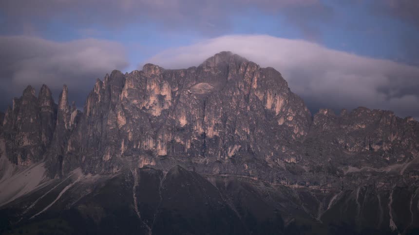 Dusk to night timelapse captures clouds swirling around the imposing peaks of a mountain range