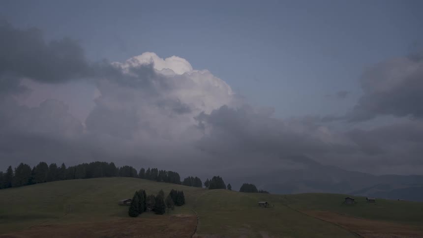 A dramatic timelapse captures a massive storm cloud forming and darkening over a serene green alpine pasture