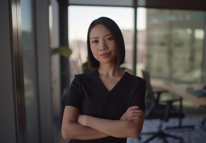 Portrait of a confident Asian businesswoman with arms crossed looking directly at the camera in a modern sunlit office