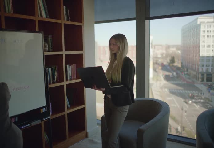 Two young professional women collaborate on a business strategy in a modern office with a large window overlooking the city