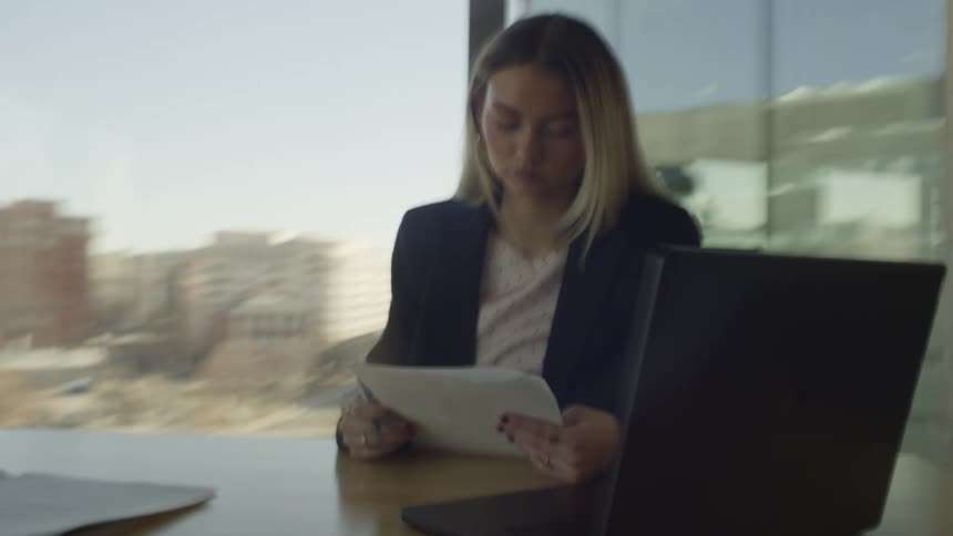 A young businesswoman in a city office diligently reviews paperwork at her desk