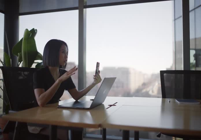 A stylish young businesswoman on a video call in a modern office, gesturing while speaking to her smartphone
