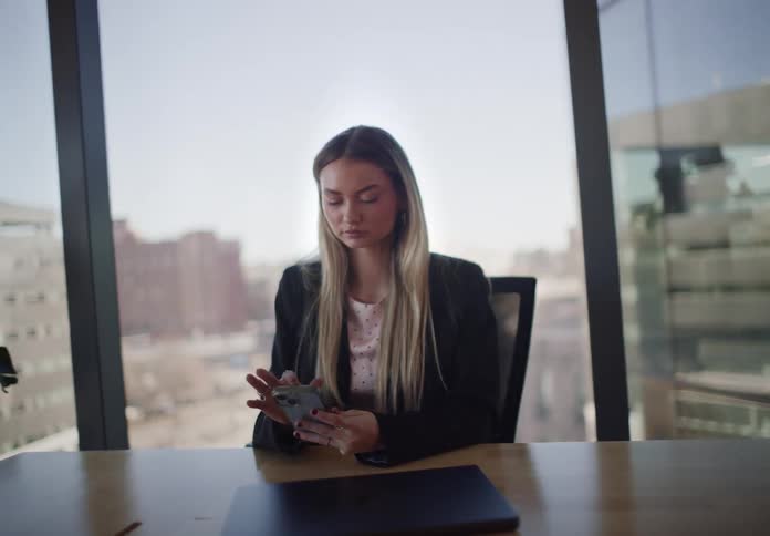 Slow dolly out shot reveals a businesswoman using her smartphone at a conference table in a modern city office