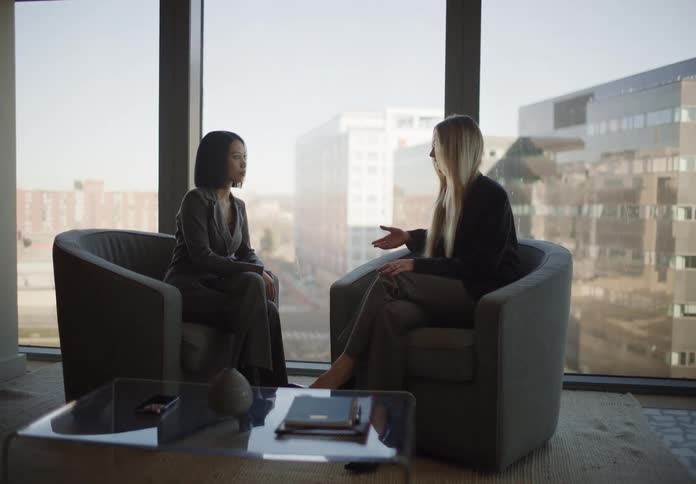 Two businesswomen have a serious discussion in a modern office with a large window overlooking the city