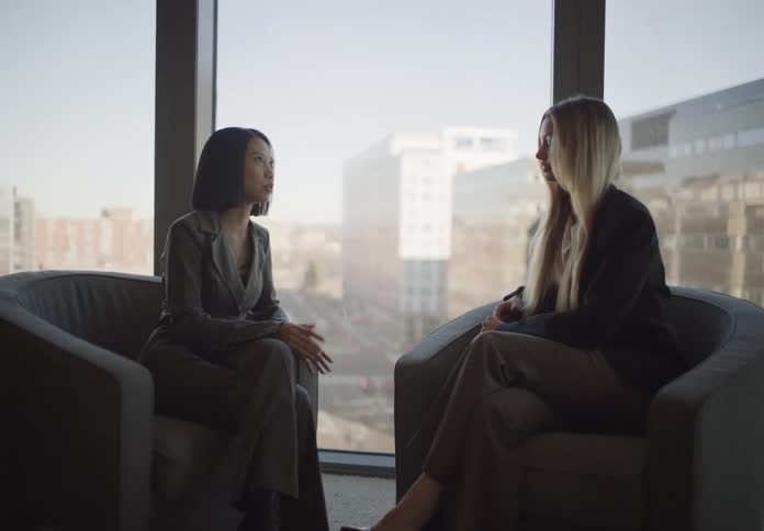 Two diverse businesswomen have an important discussion in a modern office with a large window overlooking the city