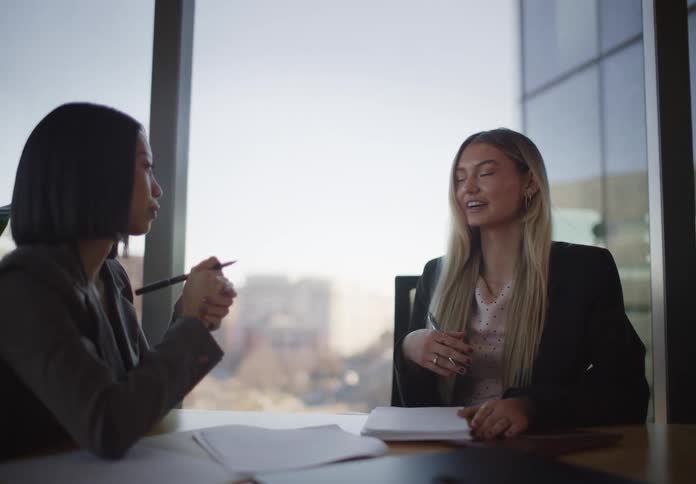 Two professional women collaborate during a business meeting in a modern conference room overlooking the city