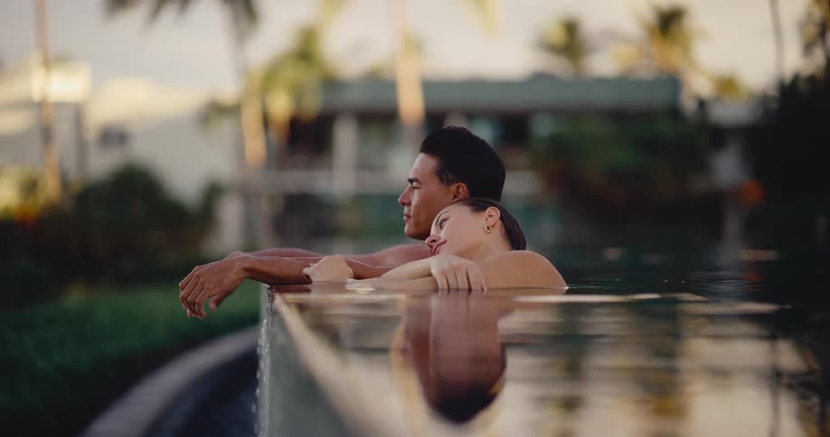 A loving couple relaxes together in an infinity pool at a luxury resort, watching the sunset