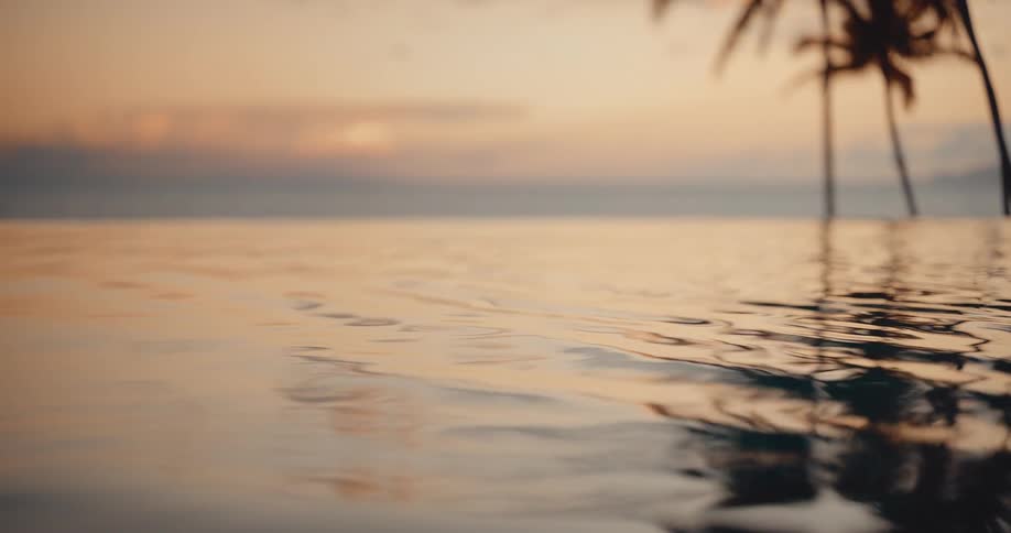 The tranquil surface of an infinity pool gently ripples, reflecting the serene colors of a tropical sunset over the ocean