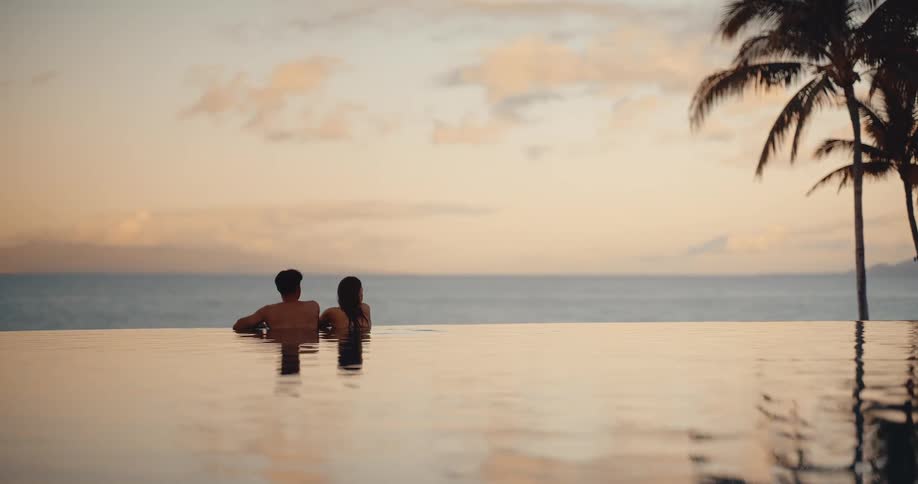 A romantic couple relaxes together in a tranquil infinity pool at sunset, enjoying the stunning ocean view from a luxury resort