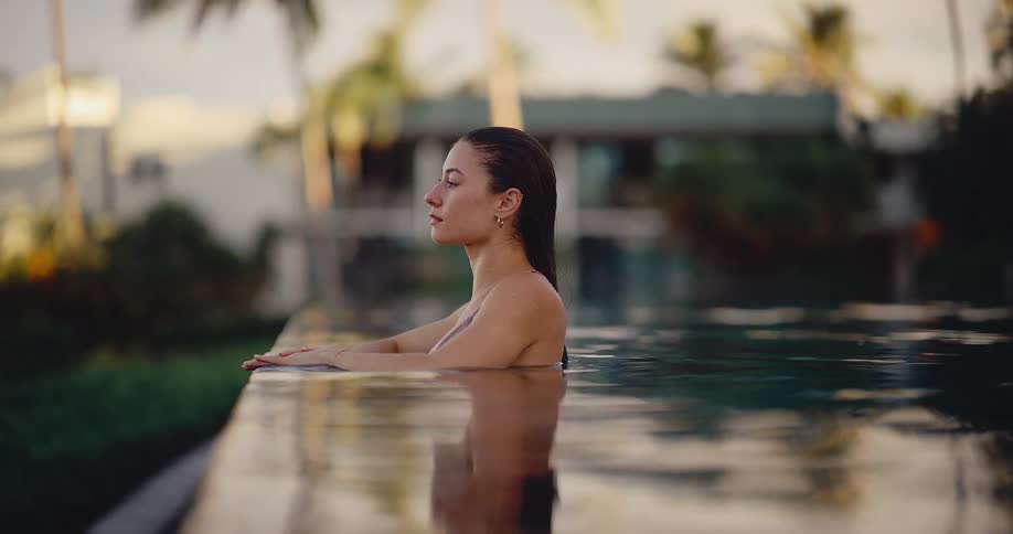 A beautiful woman finds her moment of peace and tranquility while relaxing in an infinity pool at a luxury tropical resort