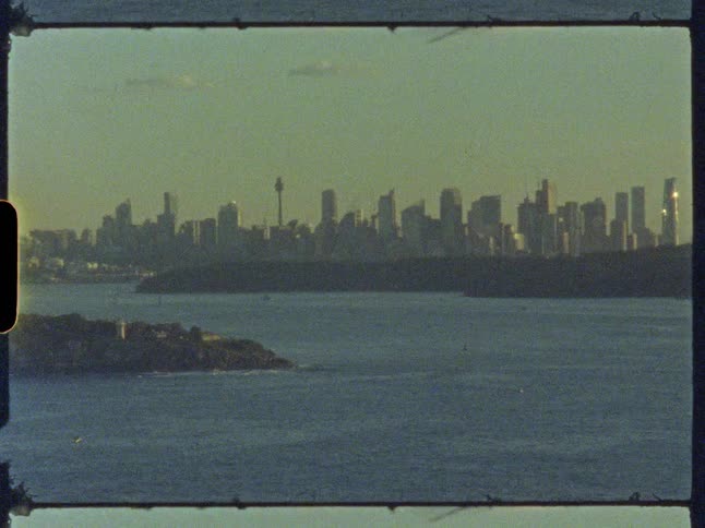 A vintage film shot captures a hazy, distant view of the Sydney, Australia skyline across the harbor