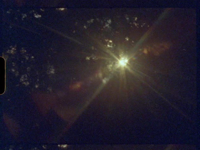 A vintage Super 8 film captures a dreamy sun flare bursting through the dark silhouette of tree leaves