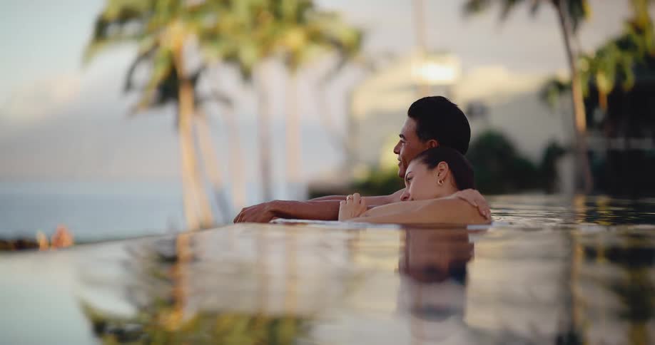 A romantic couple embraces in a tropical infinity pool at sunset