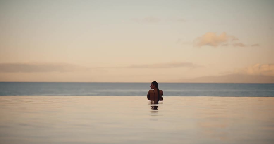 A woman relaxes in a luxurious infinity pool, enjoying the serene ocean view at sunset