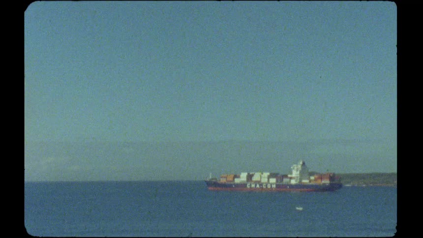 A large CMA CGM container cargo ship sails on the calm blue ocean on a clear day, captured on vintage film