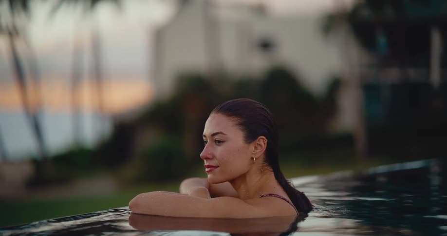 Close-up of a thoughtful young woman relaxing in a tranquil infinity pool at dusk, enjoying a serene moment on her vacation
