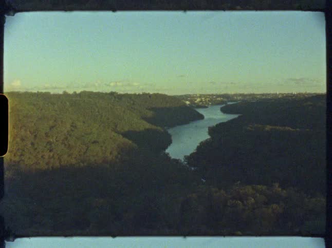 An archival, high-angle view from old film captures a serene river flowing through a forested valley