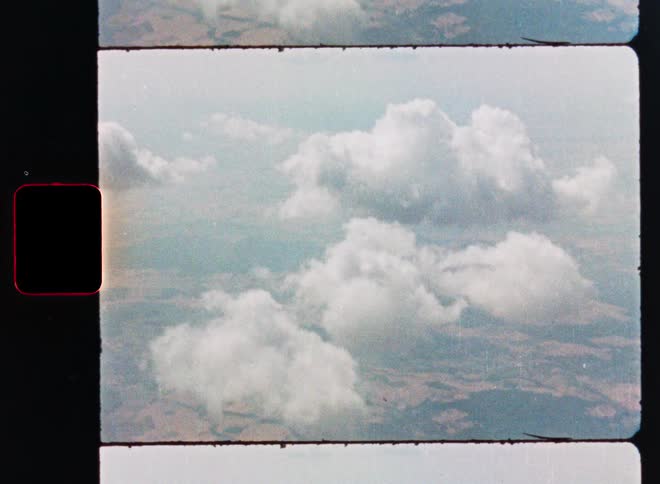 An archival 8mm film scan captures a dreamy aerial perspective of fluffy white clouds floating over the landscape