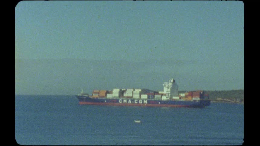 A vintage film shot captures a large CMA CGM container ship sailing across the calm ocean on a clear day