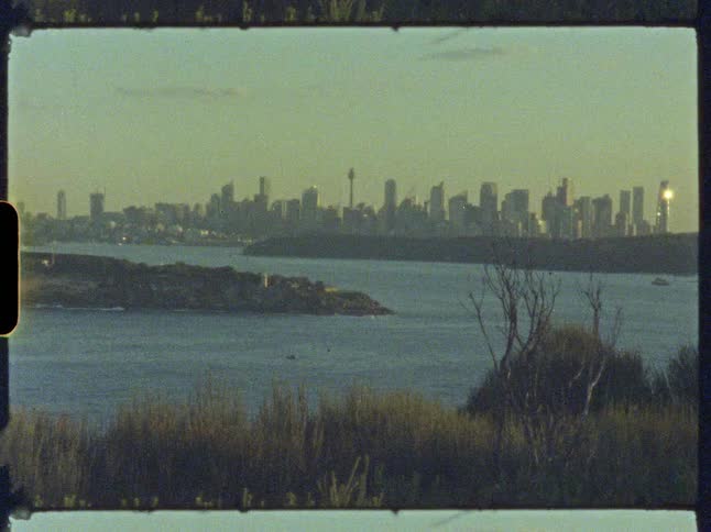 A vintage film shot captures the Sydney, Australia skyline across the harbor with an island in the foreground