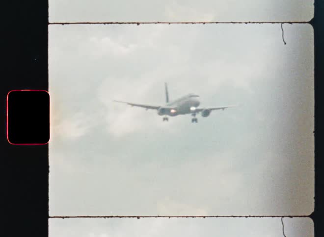 Super 8mm style footage of a passenger airplane descending from the clouds for landing