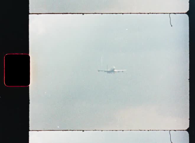 Vintage 8mm film captures a distant airplane flying towards the camera through a hazy sky