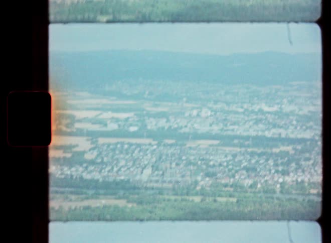A hazy, nostalgic aerial view of a European town and surrounding landscape, captured on vintage Super 8 film