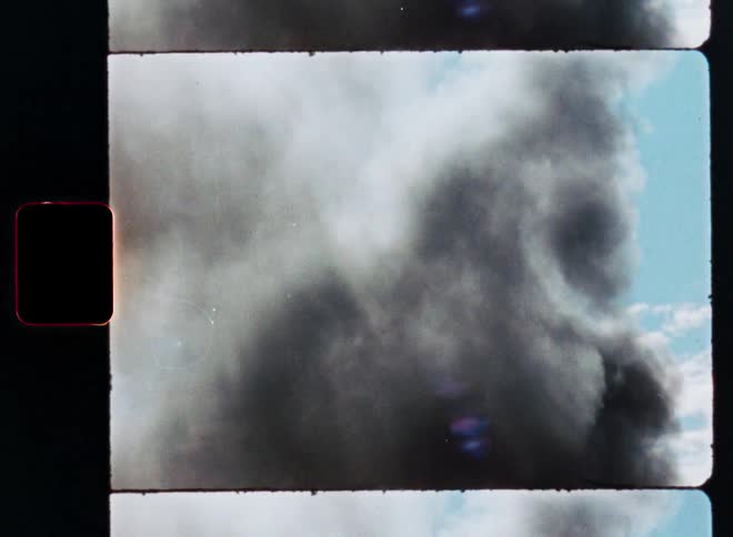 Vintage 8mm film scan shows a large plume of black smoke billowing into the blue sky from behind trees