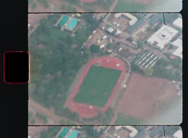 A vintage 8mm film-style aerial shot of a soccer field surrounded by a red running track
