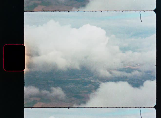 A vintage film scan captures an aerial view of clouds floating over a rural landscape seen from an airplane window