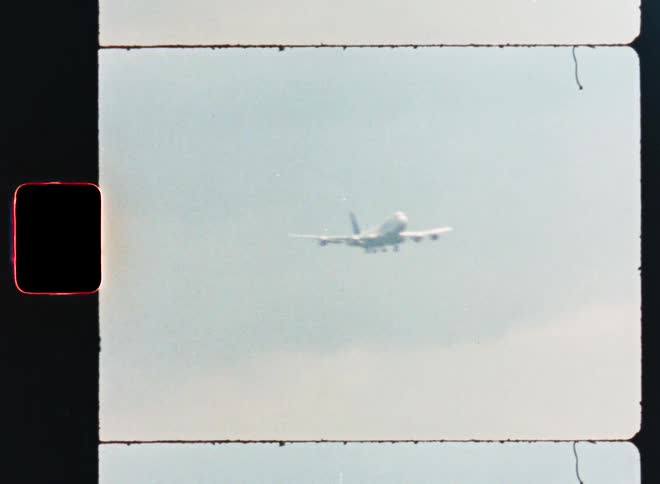 Vintage 8mm film scan captures a large passenger airplane coming in for a landing against a hazy sky
