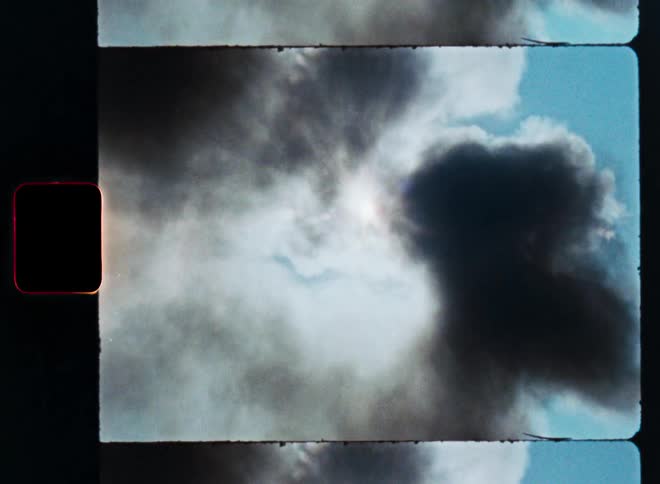Vintage film strip footage shows a plume of dark smoke rising against a bright sun in a blue sky