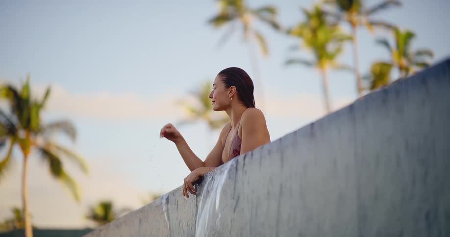 A tranquil woman in a bikini relaxes at the edge of a luxurious infinity pool with palm trees in the background