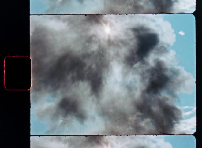 Vintage film scan of a dark plume of smoke rising into the blue sky on a sunny day