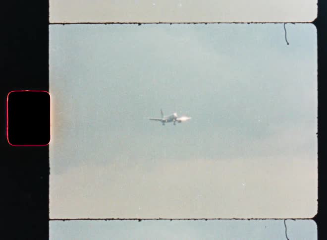 An airplane approaches for landing with its gear down, captured on vintage, grainy 8mm film
