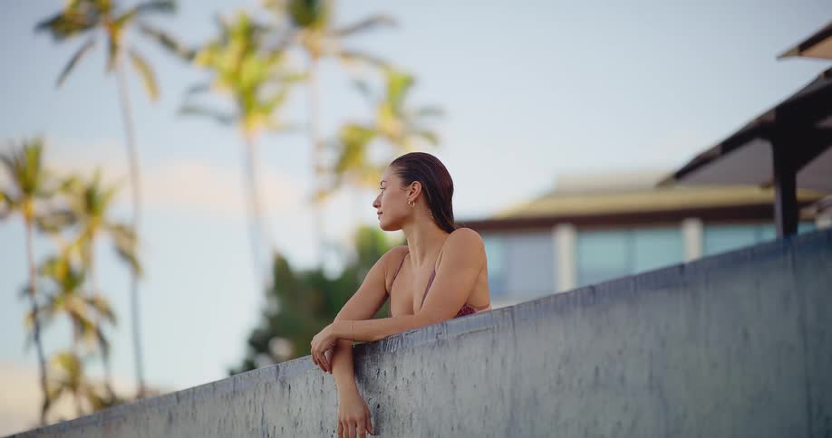 A beautiful young woman in a bikini relaxes at the edge of a luxury infinity pool, enjoying the tropical resort atmosphere