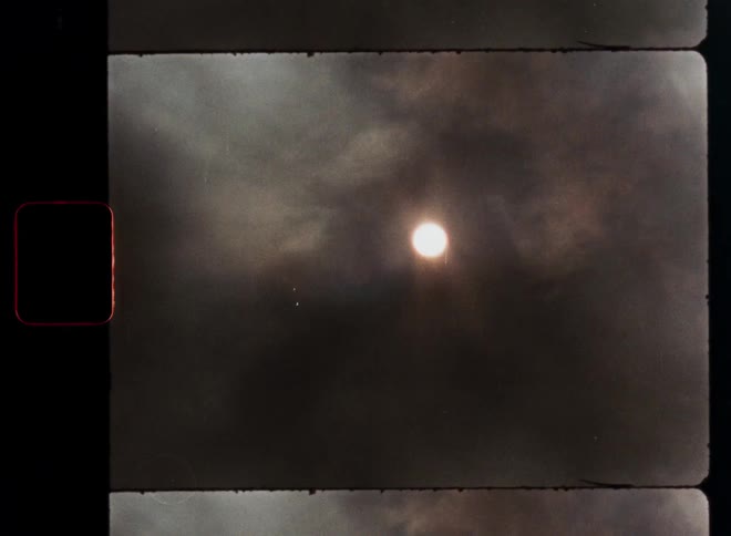 Vintage film reel captures a dramatic time-lapse of the sun emerging from behind dark, moving clouds