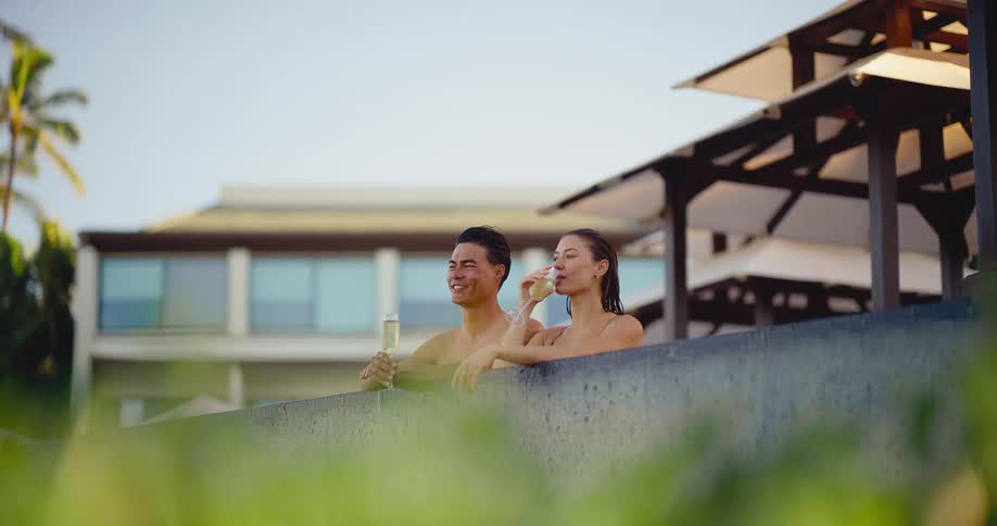 Happy young couple enjoys a celebratory glass of champagne while relaxing in the pool at a luxurious tropical resort