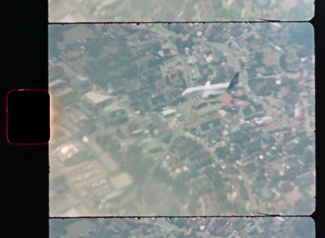 An old 8mm film captures an airplane flying over a cityscape from an aerial perspective