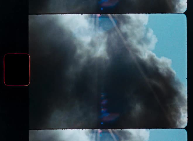 A vintage film strip shows a plume of black smoke billowing into the blue sky as the sun shines through creating a dramatic lens flare